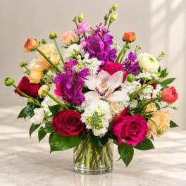 Mixed bouquet of roses, orchids, and white blooms in a glass vase