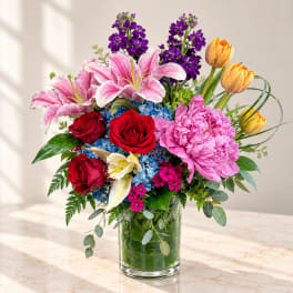 Mixed bouquet in a clear glass vase with roses, lilies, tulips, and purple blooms