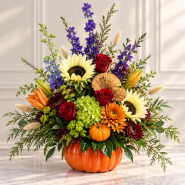 Fall bouquet in an orange pumpkin vase with sunflowers, roses, and purple blooms