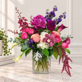 Mixed bouquet of pink, purple, and white flowers in a clear glass vase