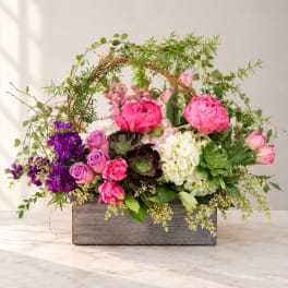 Mixed pink and purple flowers arranged in a wooden box with greenery