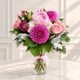 Pink and magenta bouquet in a clear glass vase with a pink ribbon