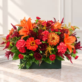Orange lilies and red mixed flowers arranged in a dark green box