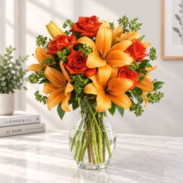 Orange lilies and red roses arranged in a clear glass vase