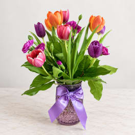 Colorful tulips and carnations in a purple vase with a ribbon