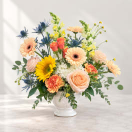 Mixed bouquet of peach, yellow, and blue flowers in a white vase