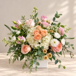 Mixed bouquet of peach and pink roses in a white vase
