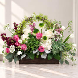 Mixed pink and white flowers arranged in a wooden box with a vine arch