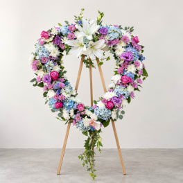 Heart-shaped floral wreath on a wooden easel with white lilies and pastel blooms