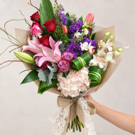 Handheld bouquet of pink lilies, roses, purple flowers, and hydrangea