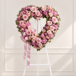 Heart-shaped pink floral wreath on a white easel with ribbon
