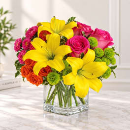 Bright mixed bouquet with yellow lilies, pink roses, and orange spray roses in a glass vase