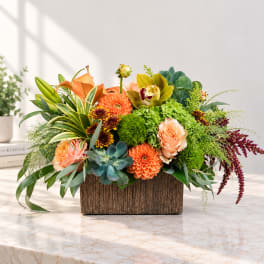 Mixed floral arrangement in a rectangular wooden container with orange and green blooms