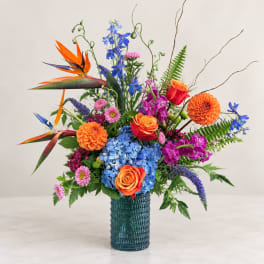 Colorful mixed bouquet in a textured blue vase with orange roses and blue hydrangea
