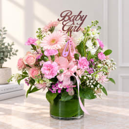 Pink and white floral arrangement in a glass vase with a "Baby Girl" topper
