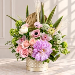 Pink and lavender floral arrangement in a polka-dot box with tall leaves