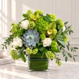 Green and white floral arrangement in a square glass vase with succulents and roses