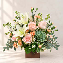 Pink roses and white lilies arranged in a square vase with a succulent