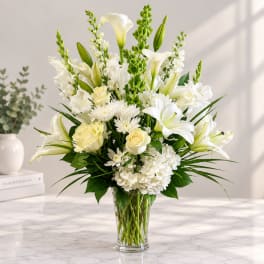 White lilies, roses, and chrysanthemums arranged in a clear glass vase