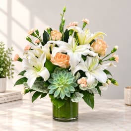 White lilies and peach roses in a glass vase with a succulent accent