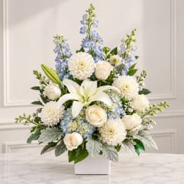 White lilies, roses, and blue flowers arranged in a white vase