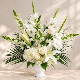 White floral arrangement in a white vase with lilies and roses