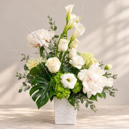 White floral arrangement in a textured white vase with calla lilies and roses
