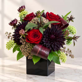 Red roses and dark purple flowers in a black square vase