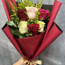 Bouquet of red, white, and pink roses wrapped in burgundy paper