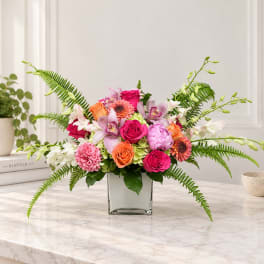 Mixed pink and orange flowers arranged in a square glass vase