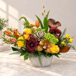 Mixed floral arrangement in a white textured bowl with yellow roses and orange blooms