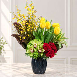Yellow tulips, red roses, and green orchids in a dark vase