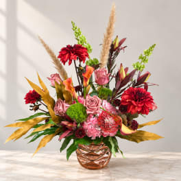 Mixed floral arrangement in a copper vase with red, pink, and orange blooms