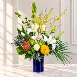 Tall mixed bouquet of white lilies and yellow orchids in a blue vase