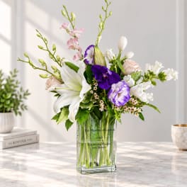 Mixed bouquet of lilies, orchids, and roses in a clear glass vase