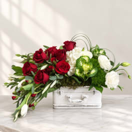 Red roses and white flowers arranged in a white suitcase-style container