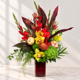 Bright tropical bouquet in a red glass vase with yellow orchids and red blooms