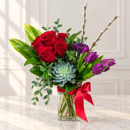 Red roses and purple tulips in a glass vase with a red ribbon