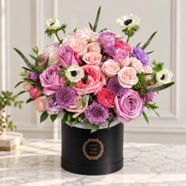 Pink and lavender roses with purple blooms in a black hatbox