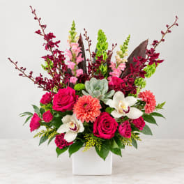 Bright mixed floral arrangement in a white square vase with roses and orchids