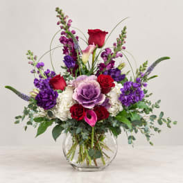 Mixed bouquet of red, purple, and white flowers in a clear glass vase
