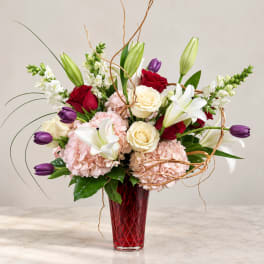 Mixed bouquet of roses, lilies, hydrangeas, and tulips in a red vase