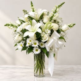 White lilies and daisies arranged in a clear glass vase with a white ribbon
