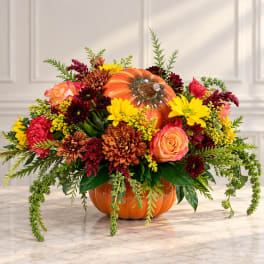 Fall floral arrangement in a pumpkin-shaped container with roses and mums