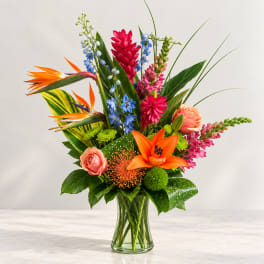 Tropical bouquet in a clear glass vase with orange lilies and pink blooms