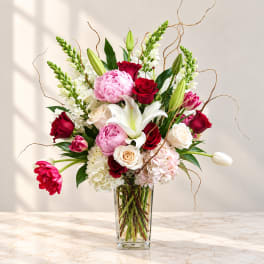 Mixed bouquet of roses, lilies, peonies, and hydrangeas in a clear glass vase