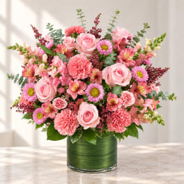 Pink mixed flower arrangement in a green glass vase