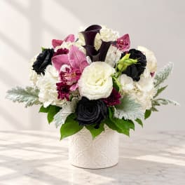 White and black floral arrangement in a white vase with pink accents