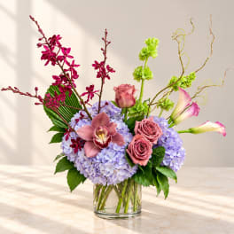 Mixed bouquet in a clear glass vase with pink orchids, roses, calla lilies, and lavender hydrangeas