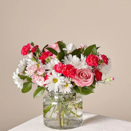 Pink roses, white daisies, and red carnations in a clear glass vase